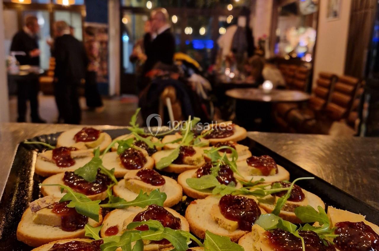 Plateau de toasts garnis de fromage, confiture et roquette, présenté dans un cadre chaleureux avec des convives en arrière…