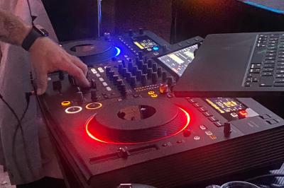Main ajustant les réglages sur une table de mixage DJ avec des lumières colorées et un ordinateur portable à proximité.