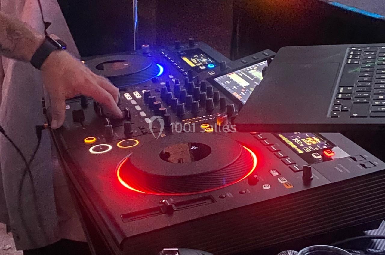 Main ajustant les réglages sur une table de mixage DJ avec des lumières colorées et un ordinateur portable à proximité.