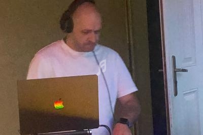 Homme portant un casque audio, debout devant un ordinateur portable avec un logo lumineux, dans une pièce intérieure.