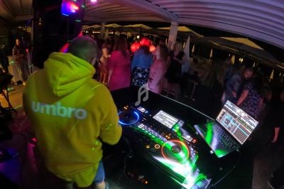 Un DJ mixe de la musique sur une table de mixage lors d'une soirée dansante sous un chapiteau éclairé.