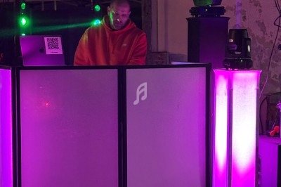 Un DJ mixe derrière une table éclairée de lumières violettes dans un environnement urbain en soirée.