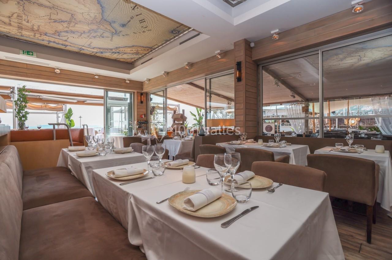 Salle de restaurant élégante avec tables dressées, nappes blanches, chaises en velours et plafond décoré d'une carte.