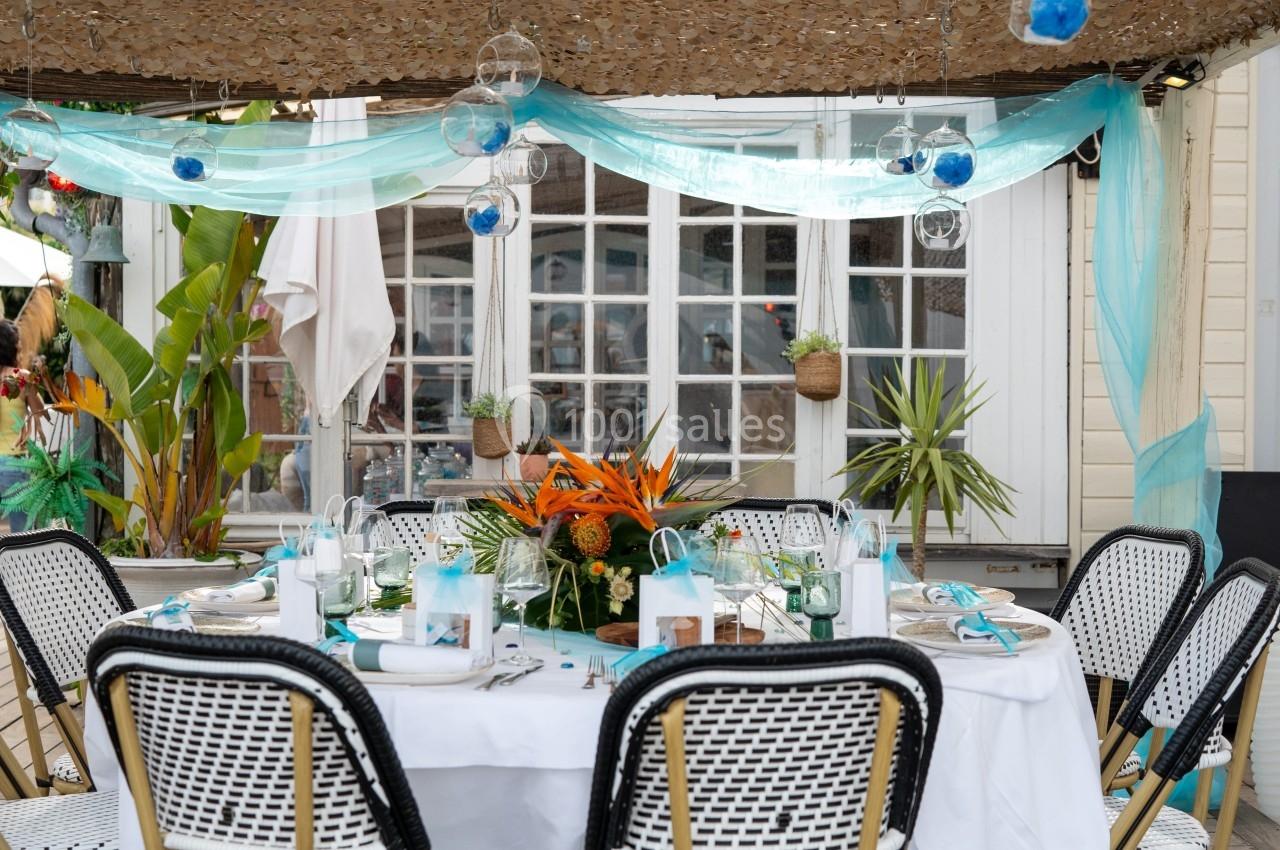 Table ronde dressée pour un repas en extérieur, décorée de fleurs orange et entourée de chaises en rotin.