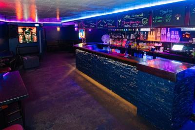 Vue intérieure d'une cellule ancienne avec murs en pierre, bancs en bois et éclairage rose.