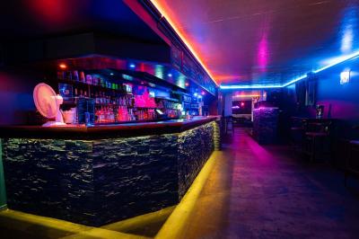 Vue intérieure d'une cellule ancienne avec murs en pierre, bancs en bois et éclairage rose.