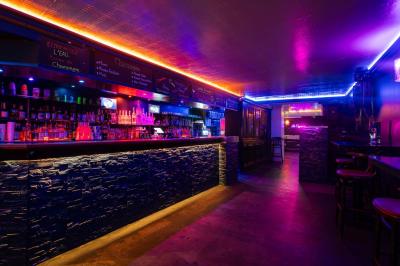 Vue intérieure d'une cellule ancienne avec murs en pierre, bancs en bois et éclairage rose.