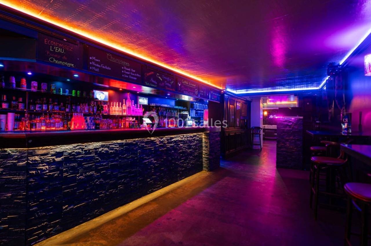 Bar avec éclairage néon coloré, comptoir en pierre, étagères de bouteilles et ambiance tamisée.