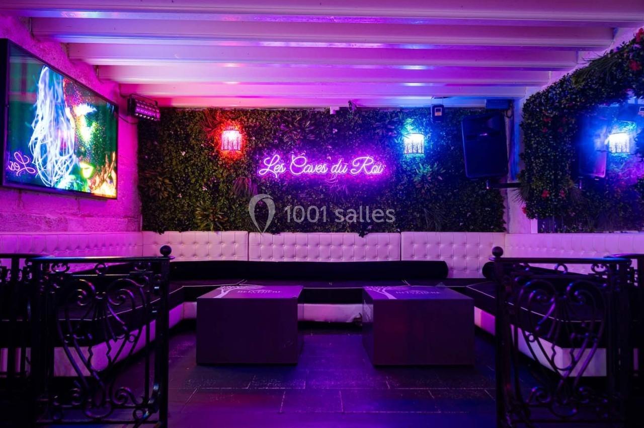 Espace lounge intérieur avec banquettes blanches, tables basses, murs végétalisés et éclairage néon coloré.