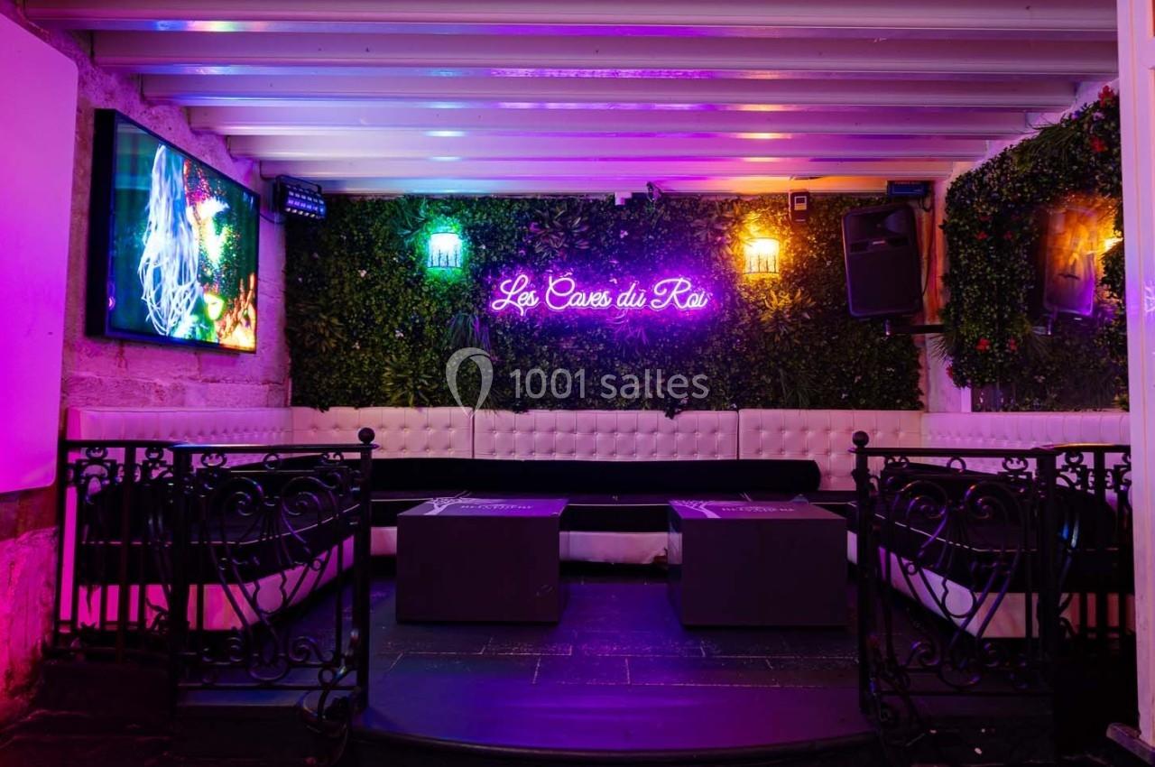 Espace lounge avec banquettes blanches, tables basses, murs végétalisés et enseigne néon colorée.