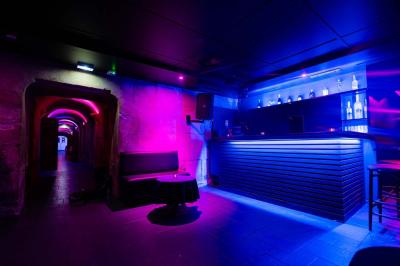 Vue intérieure d'une cellule ancienne avec murs en pierre, bancs en bois et éclairage rose.