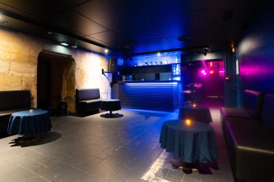 Vue intérieure d'une cellule ancienne avec murs en pierre, bancs en bois et éclairage rose.