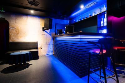 Vue intérieure d'une cellule ancienne avec murs en pierre, bancs en bois et éclairage rose.