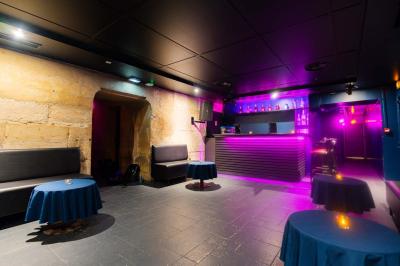 Vue intérieure d'une cellule ancienne avec murs en pierre, bancs en bois et éclairage rose.