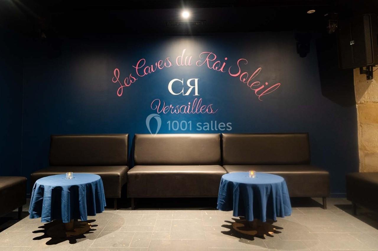 Salle avec banquettes noires, tables rondes couvertes de nappes bleues et mur bleu portant une inscription décorative.