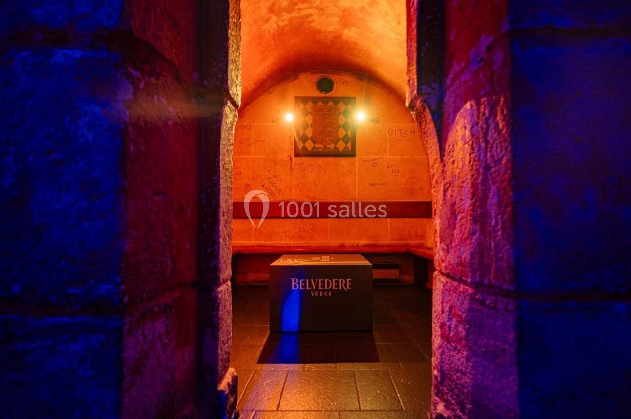 Vue d'une petite salle voûtée en pierre éclairée par des lumières colorées, avec un cube marqué ’Belvedere’ au centre.