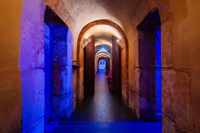 Vue intérieure d'une cellule ancienne avec murs en pierre, bancs en bois et éclairage rose.