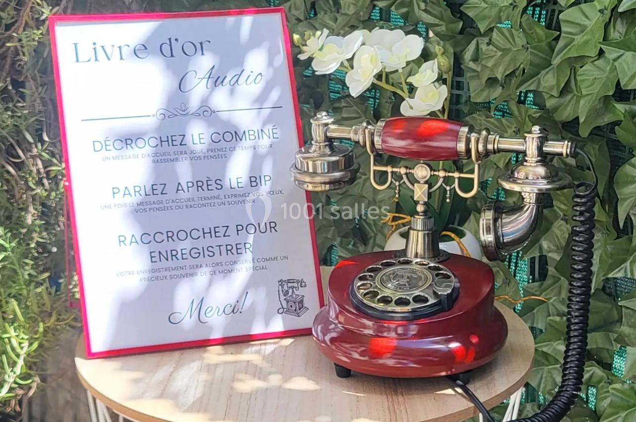 Téléphone rétro rouge posé sur une table, accompagné d'un panneau expliquant son usage comme livre d'or audio.