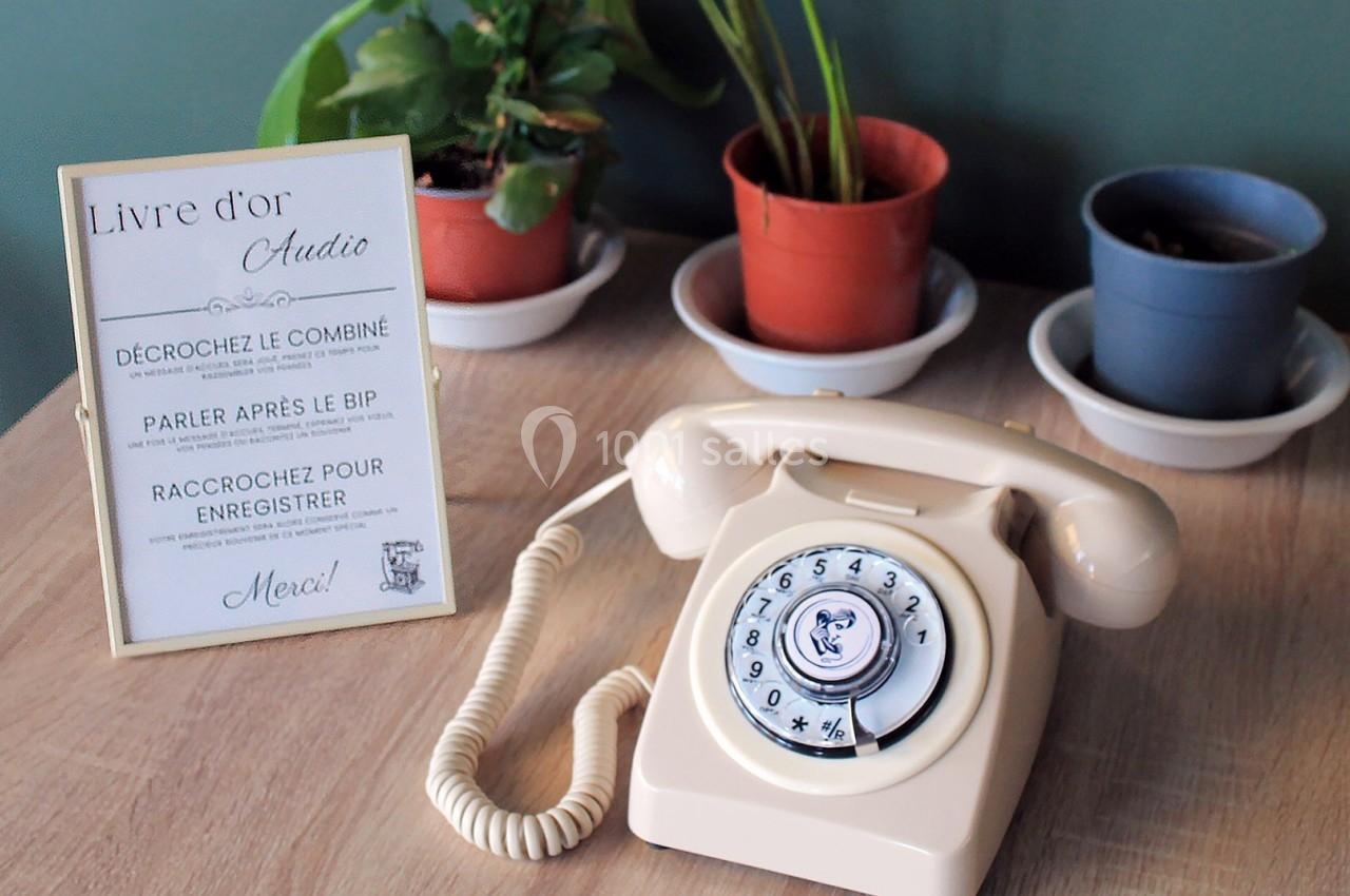 Téléphone rétro beige posé sur une table en bois, entouré de plantes en pot et d'un panneau explicatif.