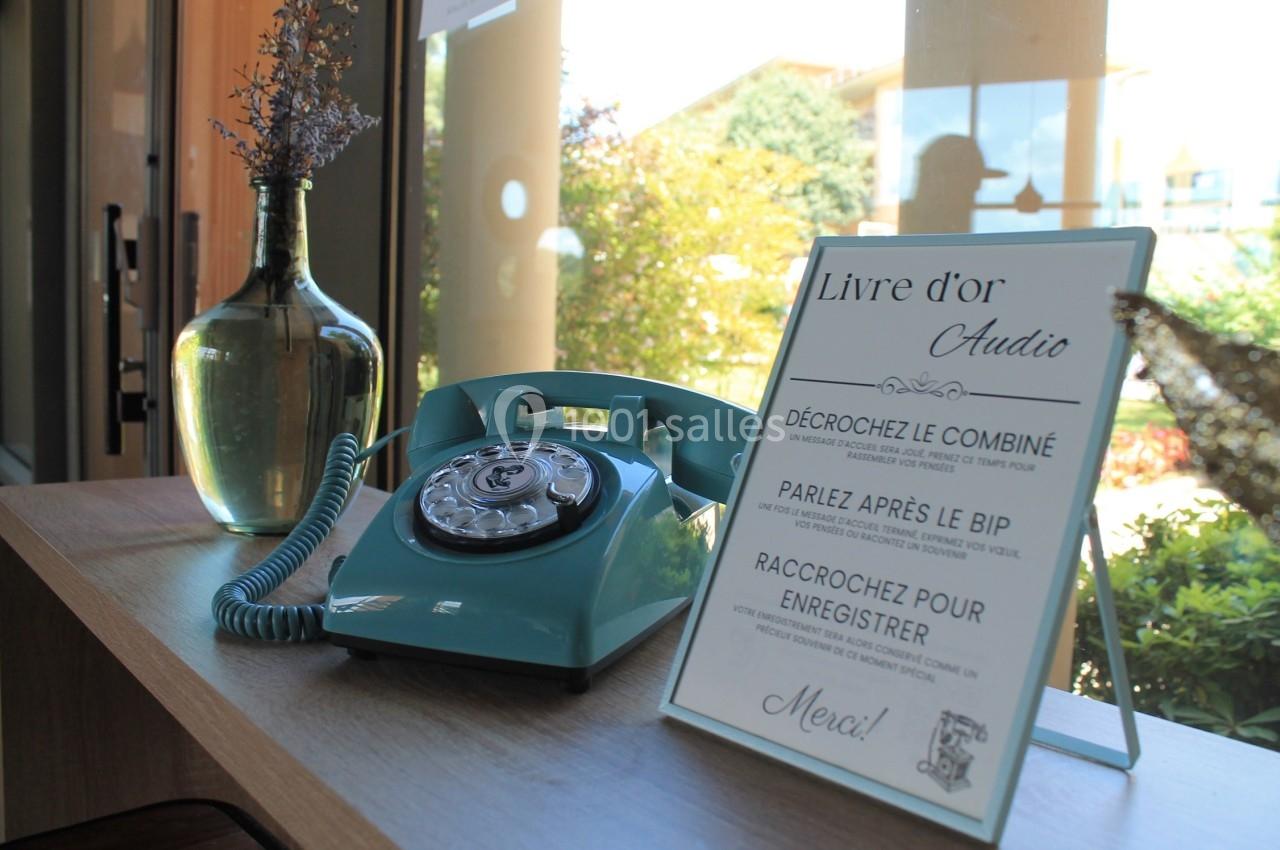 Téléphone rétro vert avec un panneau expliquant un livre d'or audio, posé sur une table près d'une fenêtre.