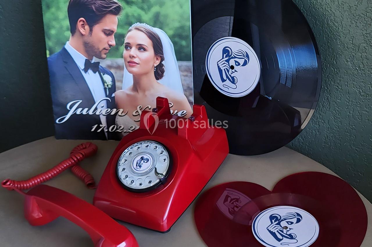 Photo d'un téléphone rouge rétro, un disque vinyle noir, un disque rouge en forme de cœur et une photo de mariage.