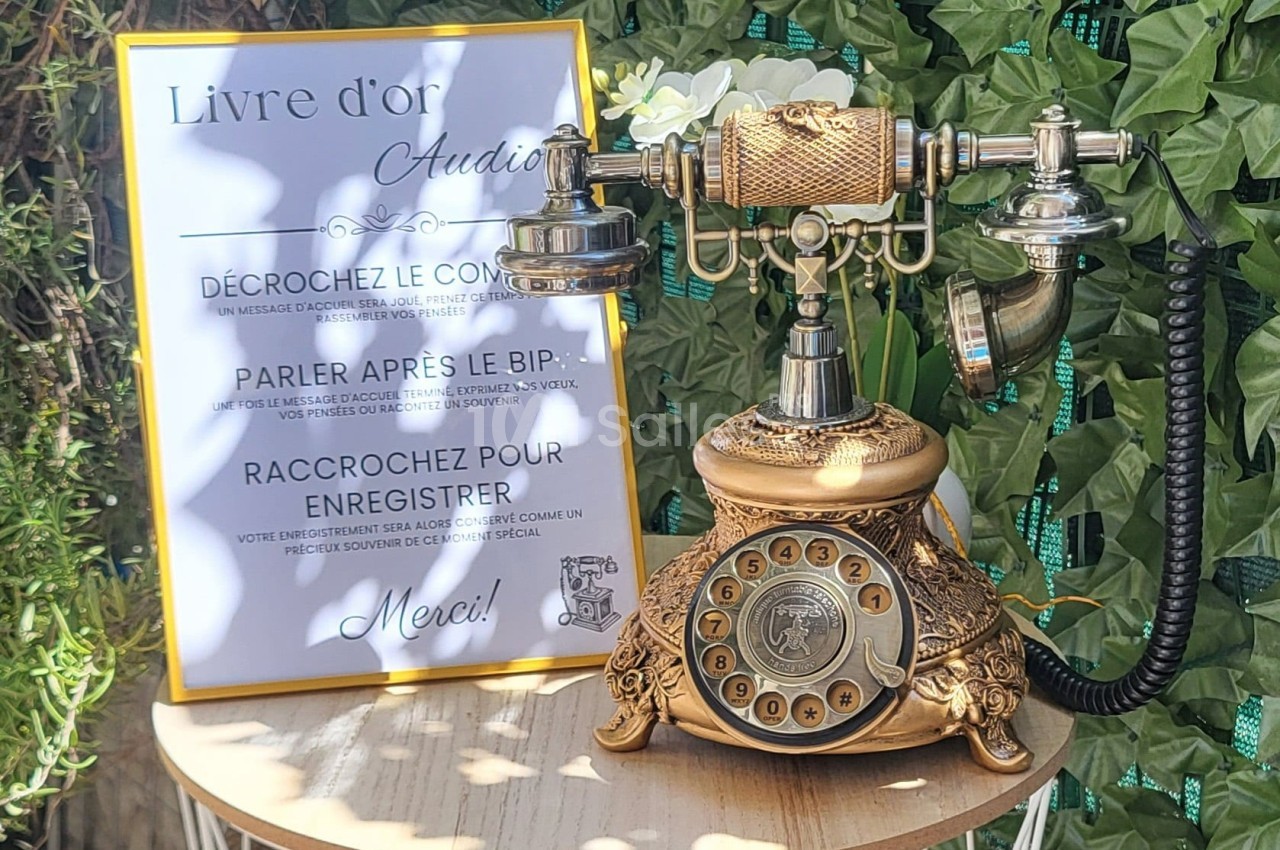Téléphone rétro doré sur une table, accompagné d'un panneau expliquant son usage comme livre d'or audio.