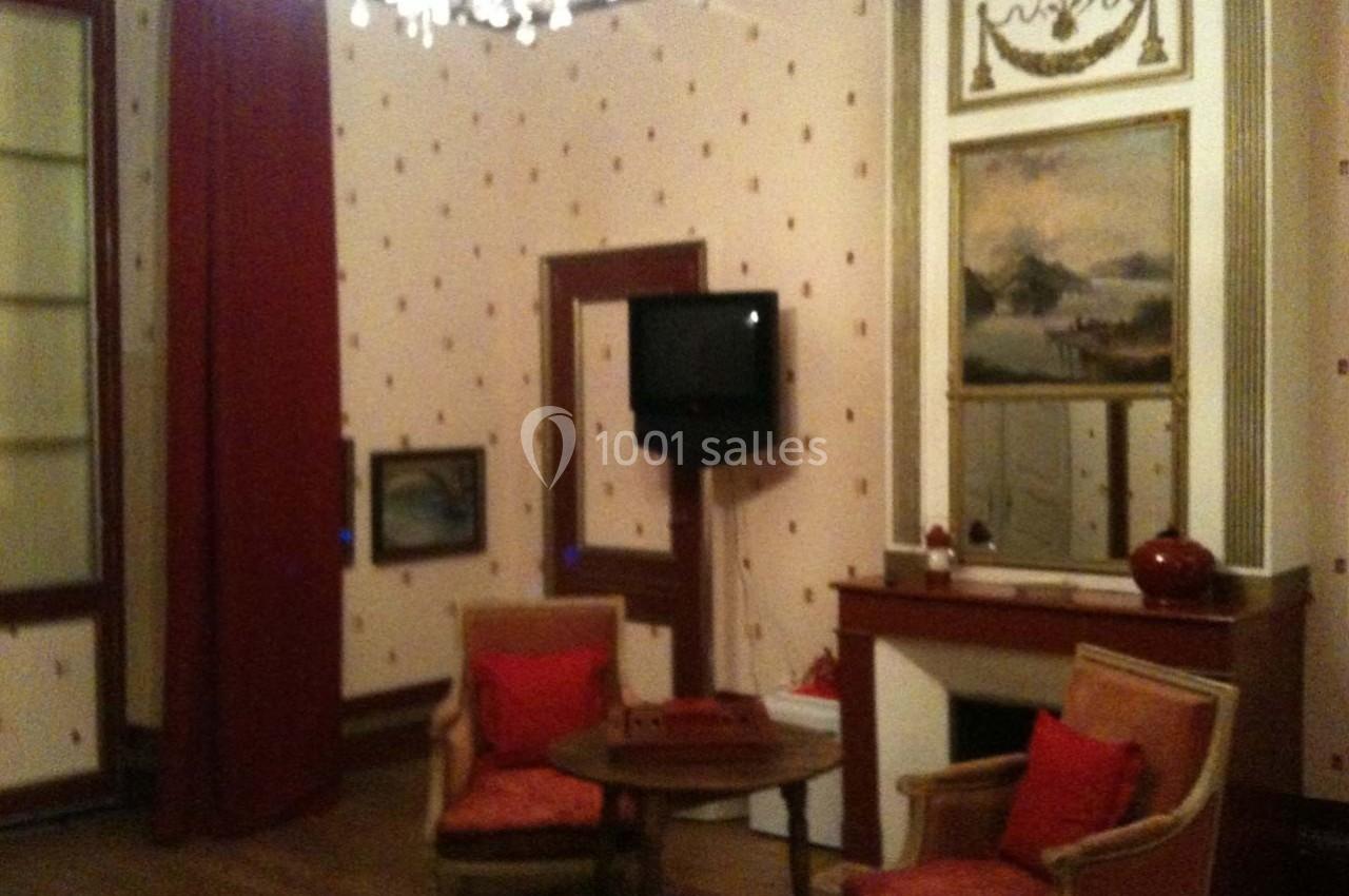 Deux fauteuils autour d'une table basse dans une pièce avec cheminée, télé murale et décoration classique.