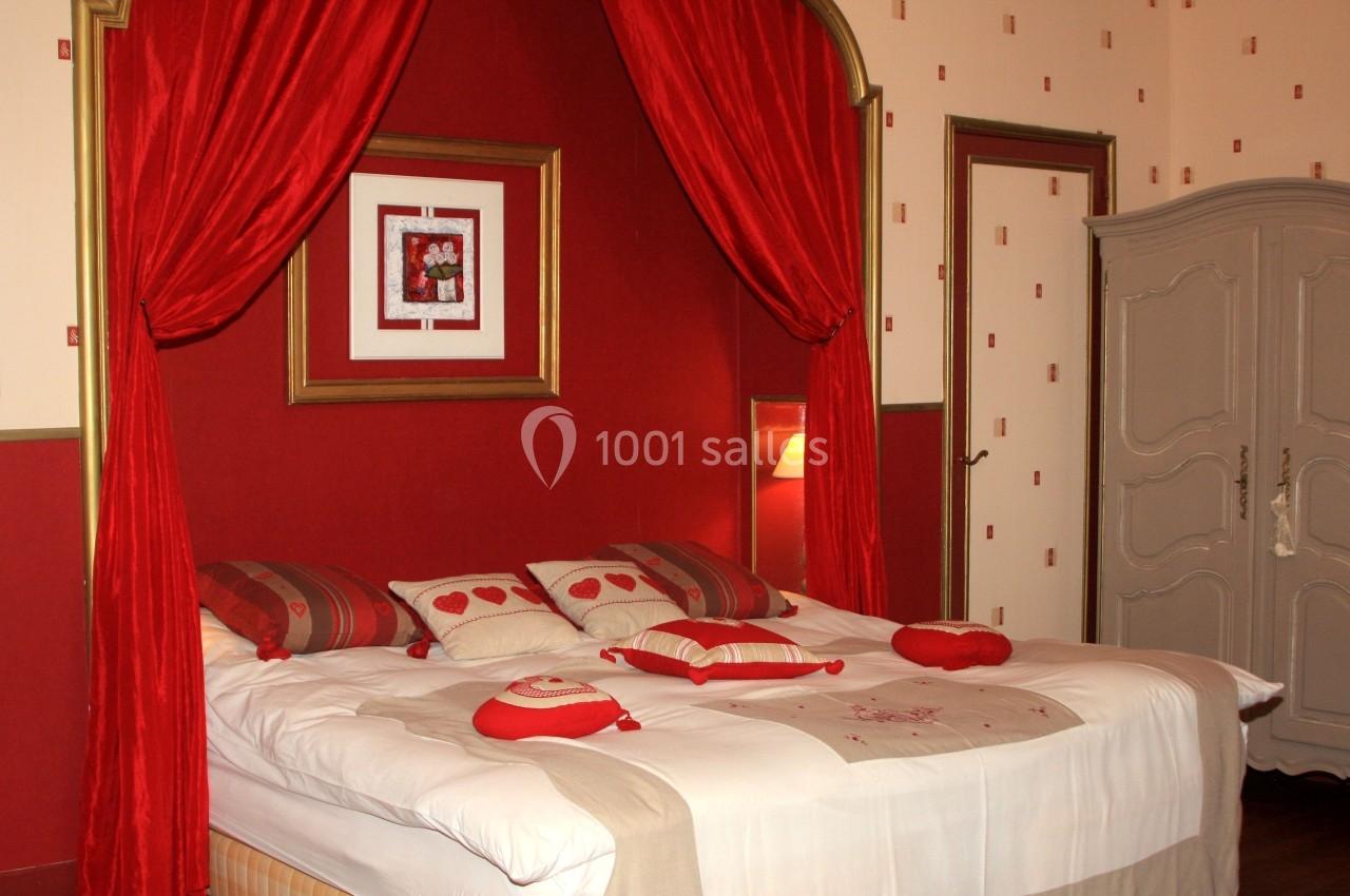 Lit double avec coussins décoratifs rouges et blancs, encadré par des rideaux rouges dans une chambre au style classique.