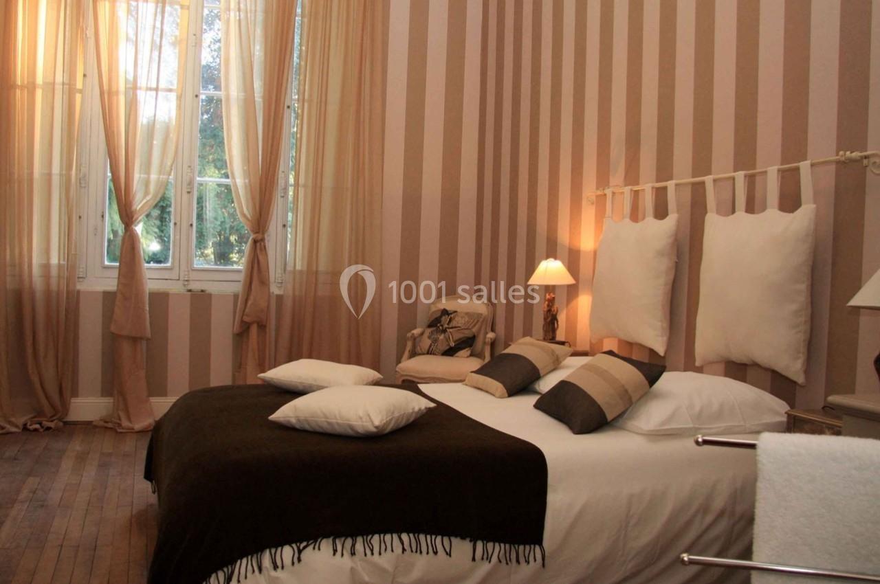 Chambre avec lit double, coussins assortis, lampes de chevet et rideaux transparents laissant entrer la lumière naturelle.