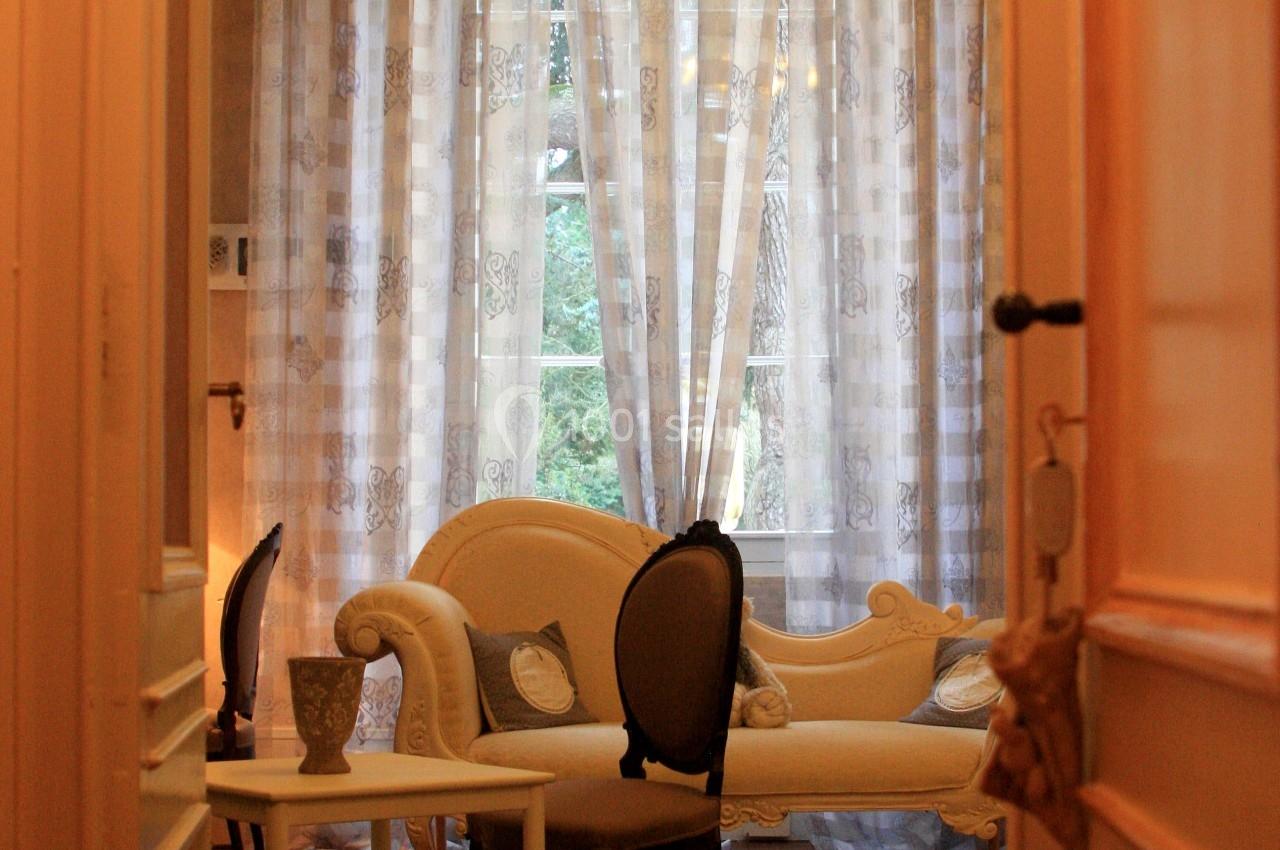 Vue d'un salon élégant avec canapé, fauteuil, table basse et rideaux transparents laissant entrevoir un jardin.