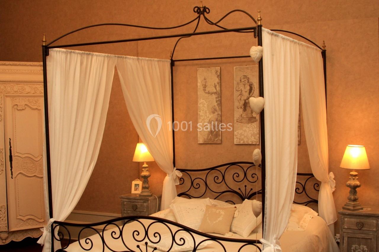 Lit à baldaquin en fer forgé avec drapés blancs, entouré de lampes de chevet et d'une armoire ancienne dans une chambre…