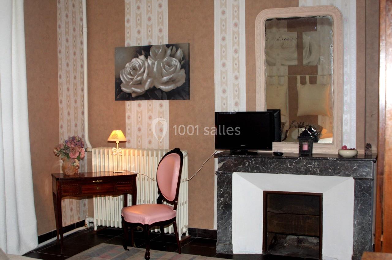 Coin d'une chambre avec un bureau en bois, une chaise rose, une cheminée, un miroir et une télévision.