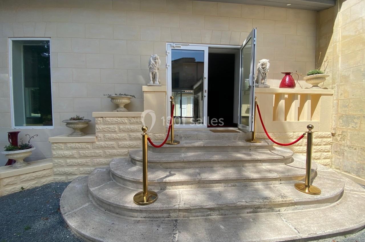 Entrée d'un bâtiment avec marches en pierre, balustrade dorée et cordons rouges, décorée de statues de lions.
