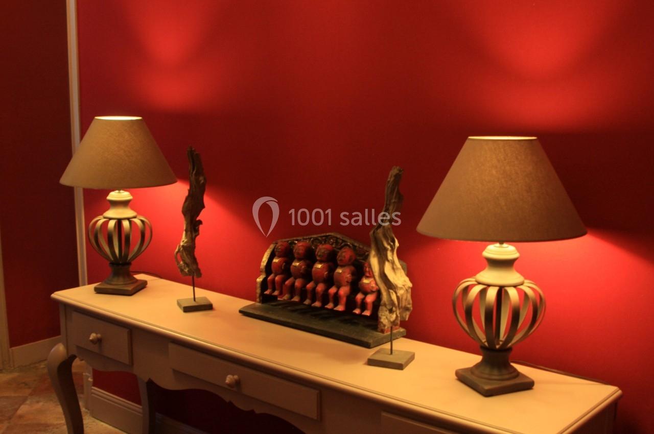 Deux lampes à abat-jour beige encadrent une décoration sculptée sur une console en bois, devant un mur rouge.