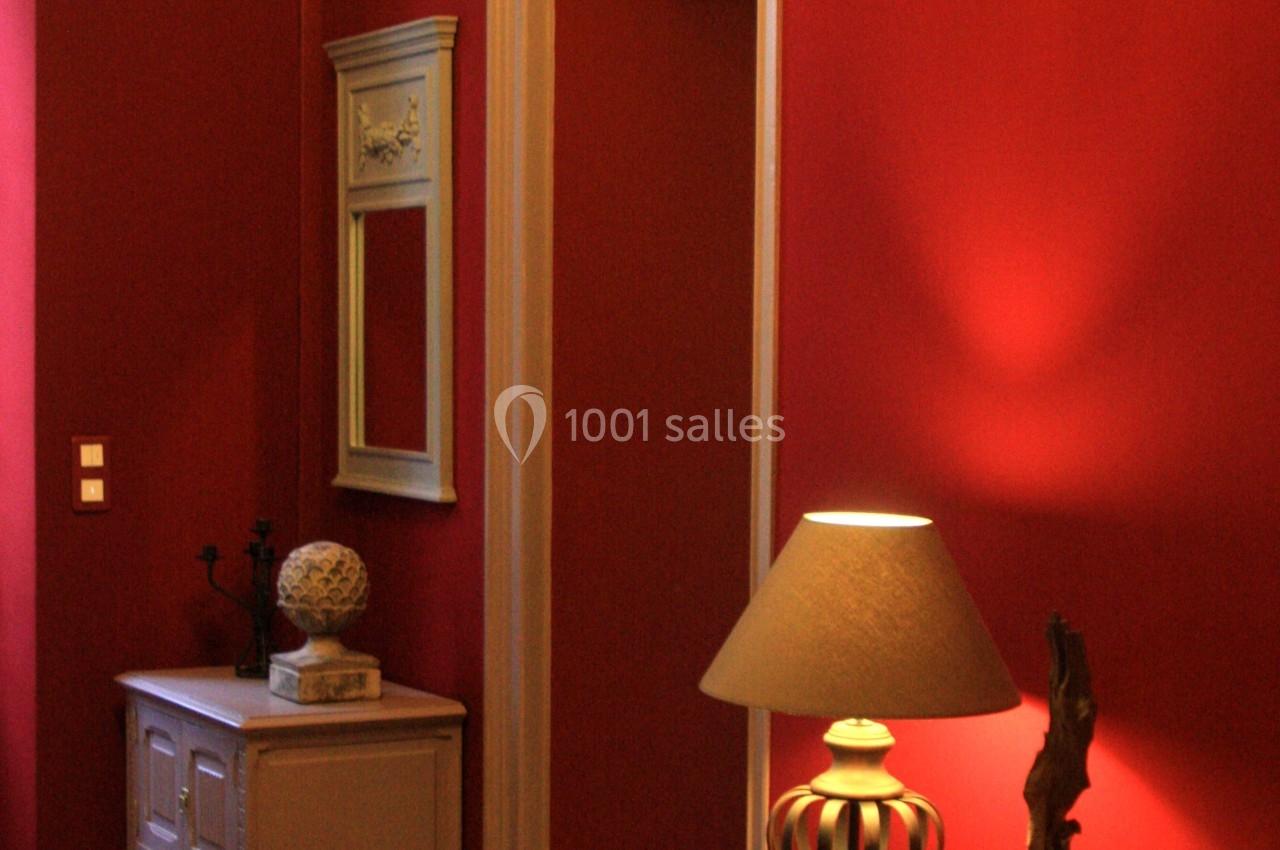 Intérieur avec murs rouges, meubles en bois clair, lampe allumée et miroir encadré au mur.