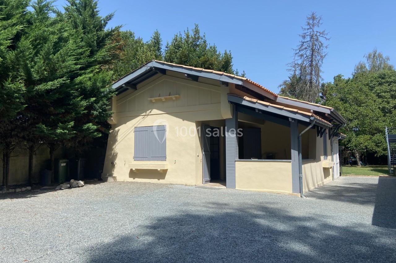 Maison individuelle de plain-pied avec façade jaune, volets gris et entourée d'arbres, sur une allée gravillonnée.