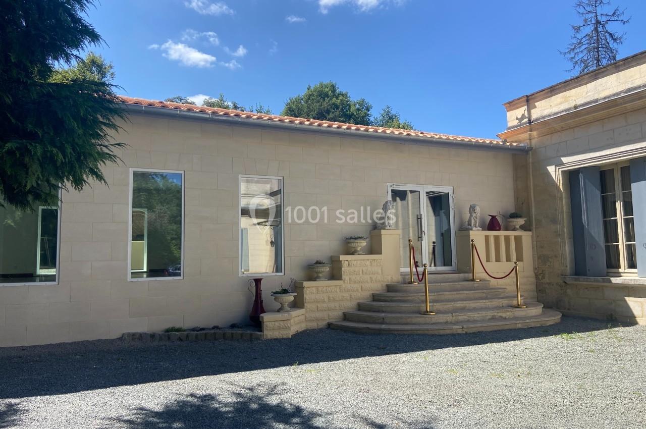Façade d'un bâtiment en pierre avec escalier central, balustrade et ciel dégagé en arrière-plan.