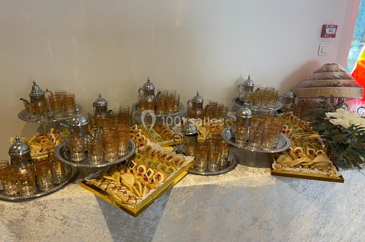 Plateau de pâtisseries et verres à thé disposés sur une table avec des théières argentées.