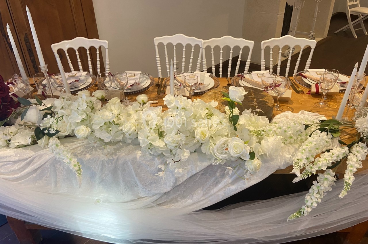 Décoration de table de réception avec nappes blanches, chandeliers, vaisselle élégante et arrangement floral blanc.