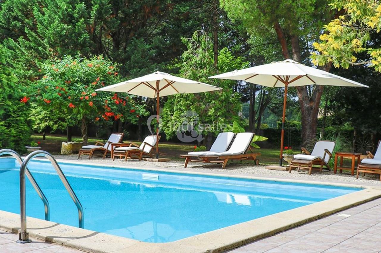 Piscine extérieure entourée de chaises longues, parasols blancs et végétation luxuriante.