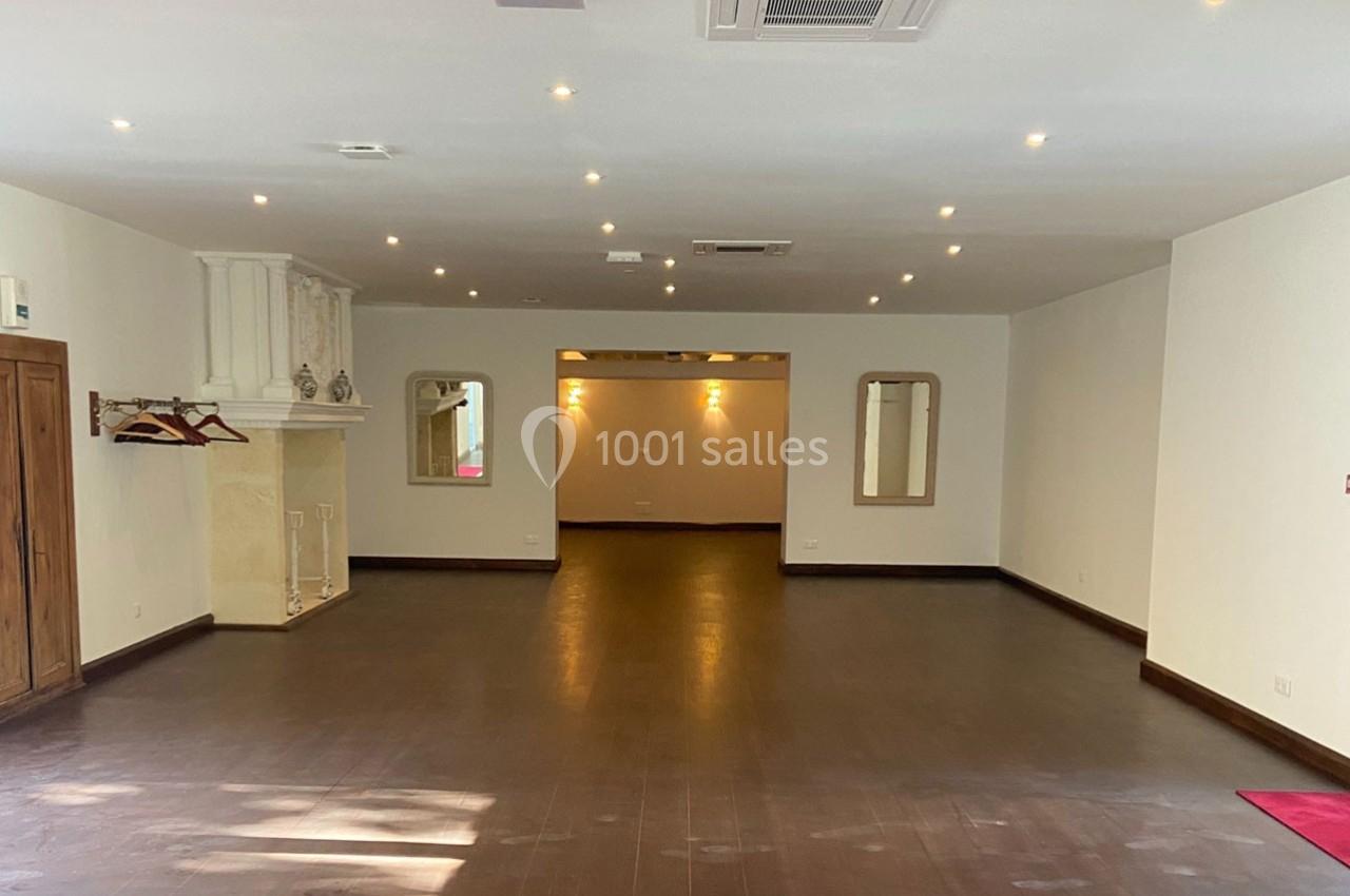 Salle vide avec parquet sombre, murs blancs, cheminée, deux miroirs et éclairage encastré au plafond.