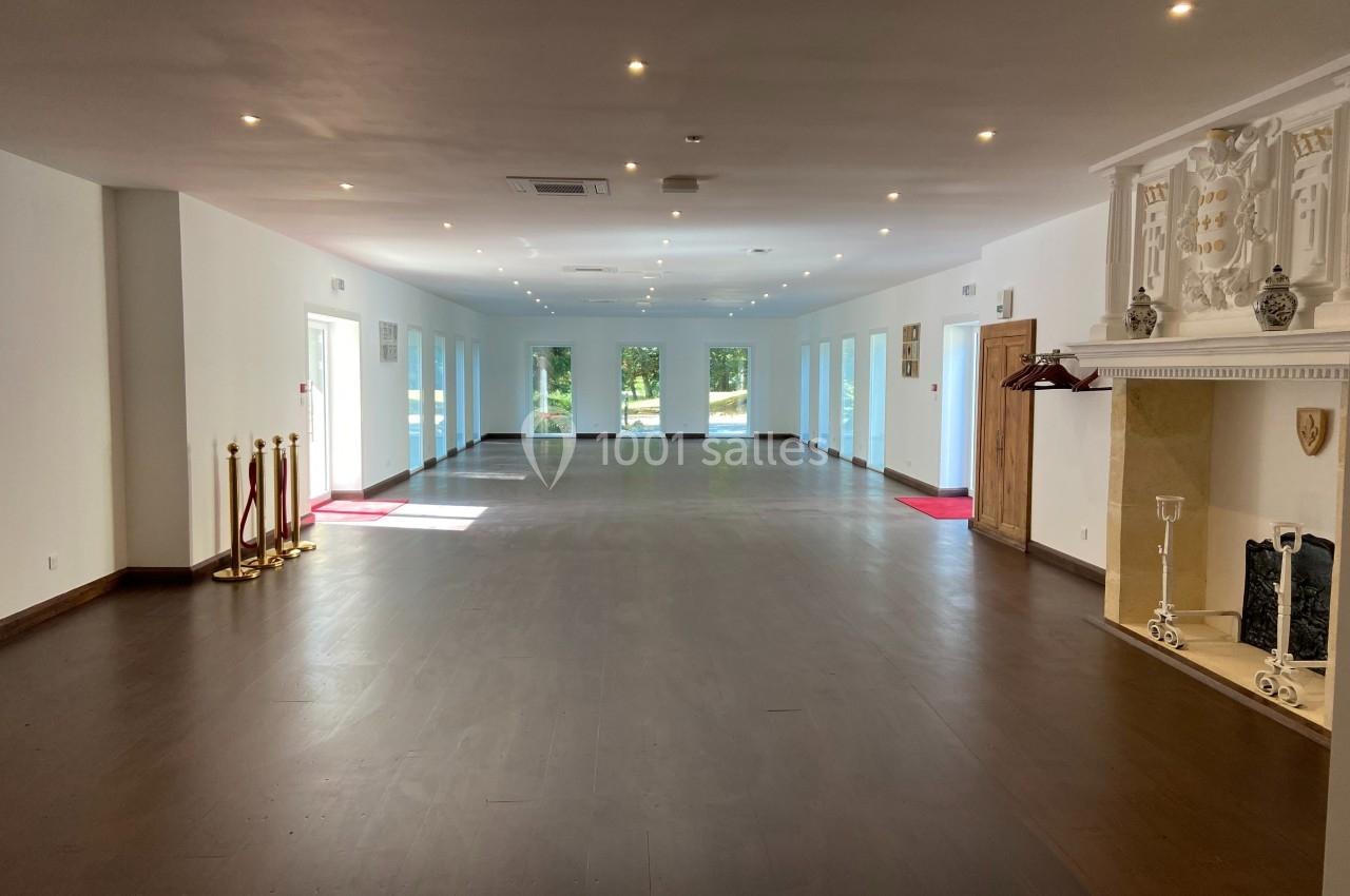 Salle spacieuse avec parquet sombre, cheminée décorative, grandes fenêtres et lumière naturelle abondante.