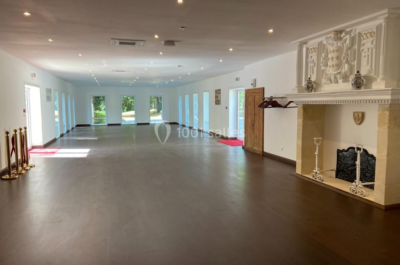 Salle spacieuse avec parquet sombre, cheminée décorative blanche et grandes fenêtres laissant entrer la lumière naturelle.