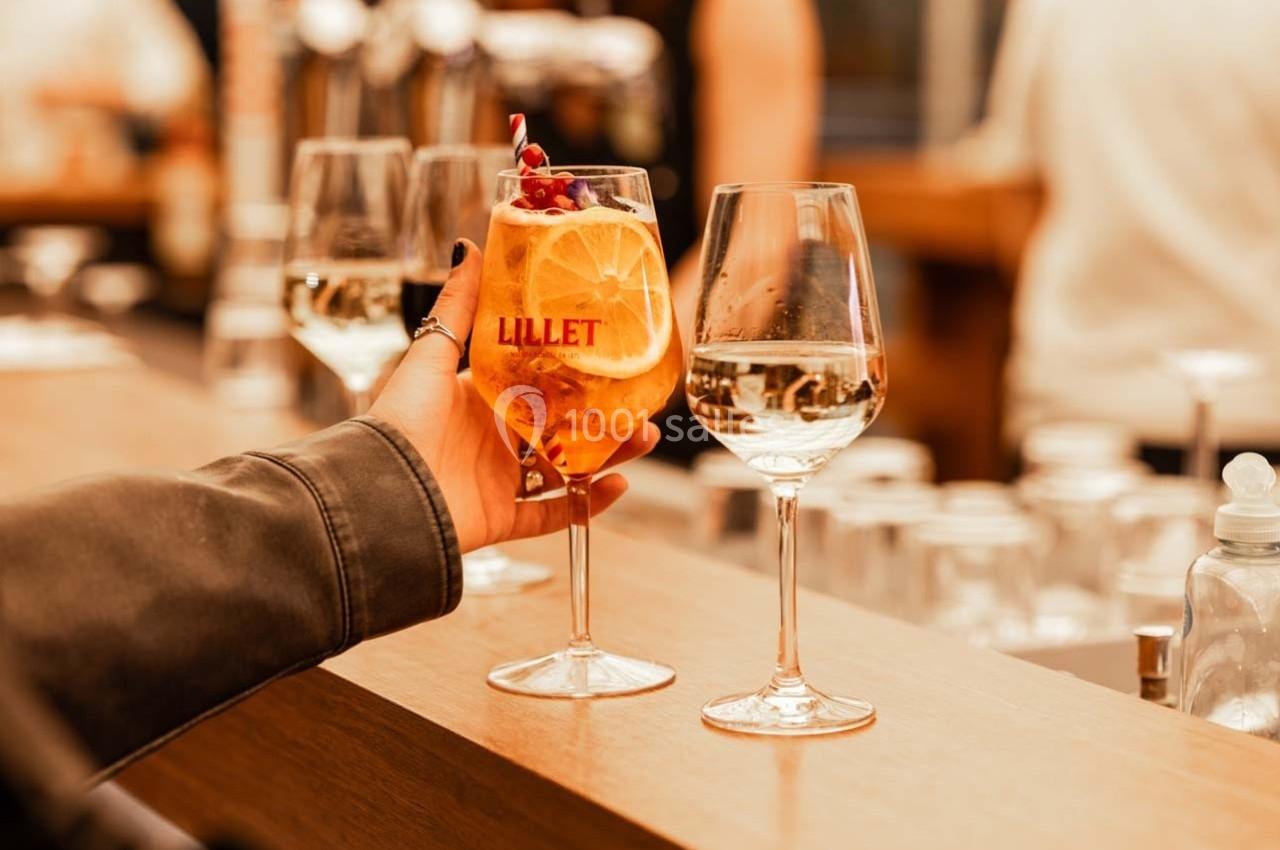 Un verre de cocktail avec une tranche d'orange et des baies, tenu par une main, posé sur un comptoir en bois.
