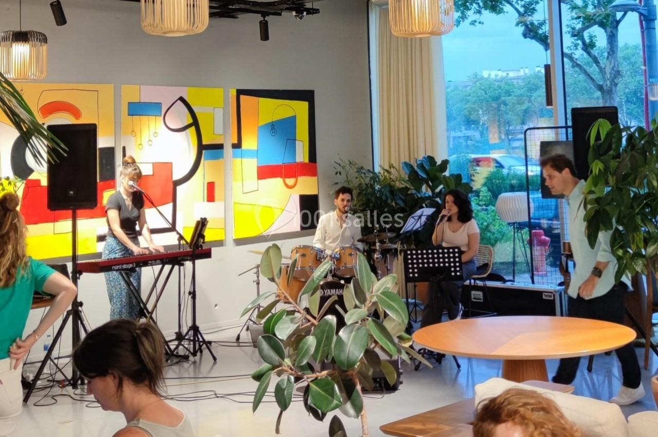 Un groupe de musiciens joue en intérieur devant un public, entouré de plantes et de décorations modernes.