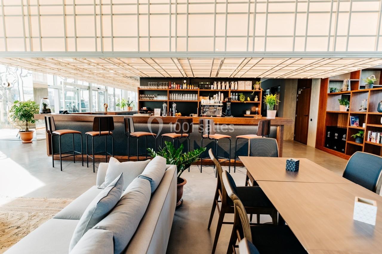 Espace intérieur lumineux avec un bar, des tables, des chaises et des plantes, dans un décor moderne et épuré.