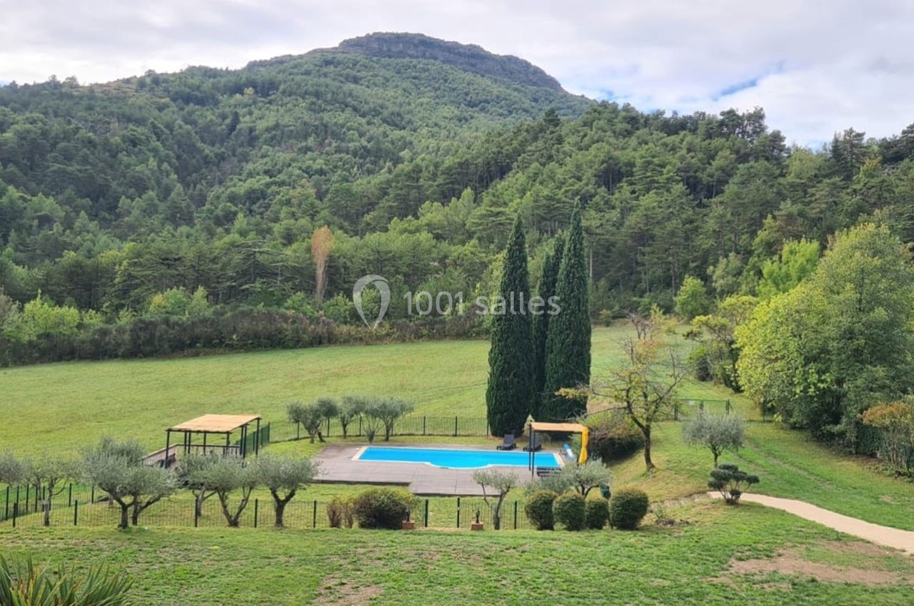 Vue d'une piscine entourée de verdure, avec des arbres et des collines boisées en arrière-plan.