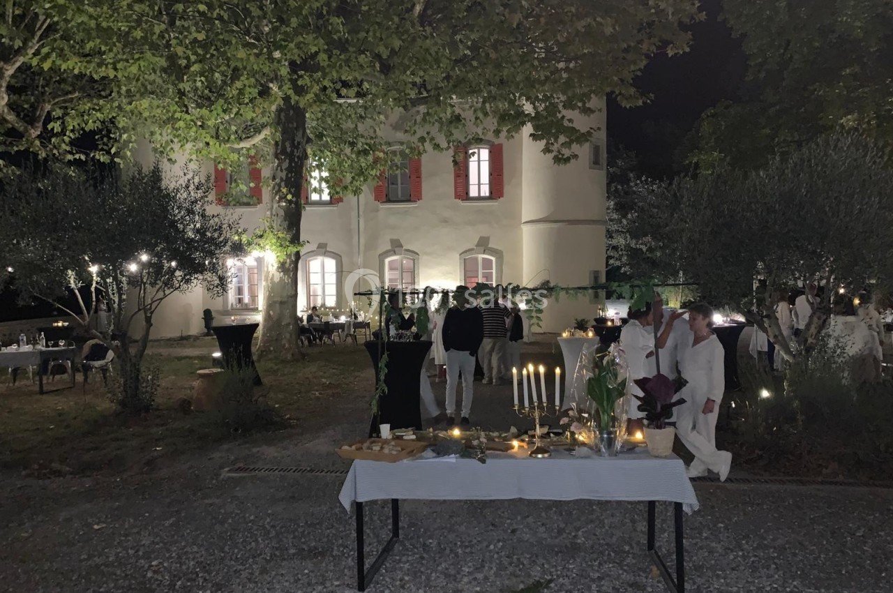 Table dressée avec des bougies et des plats devant une maison éclairée, lors d'un événement nocturne en extérieur.
