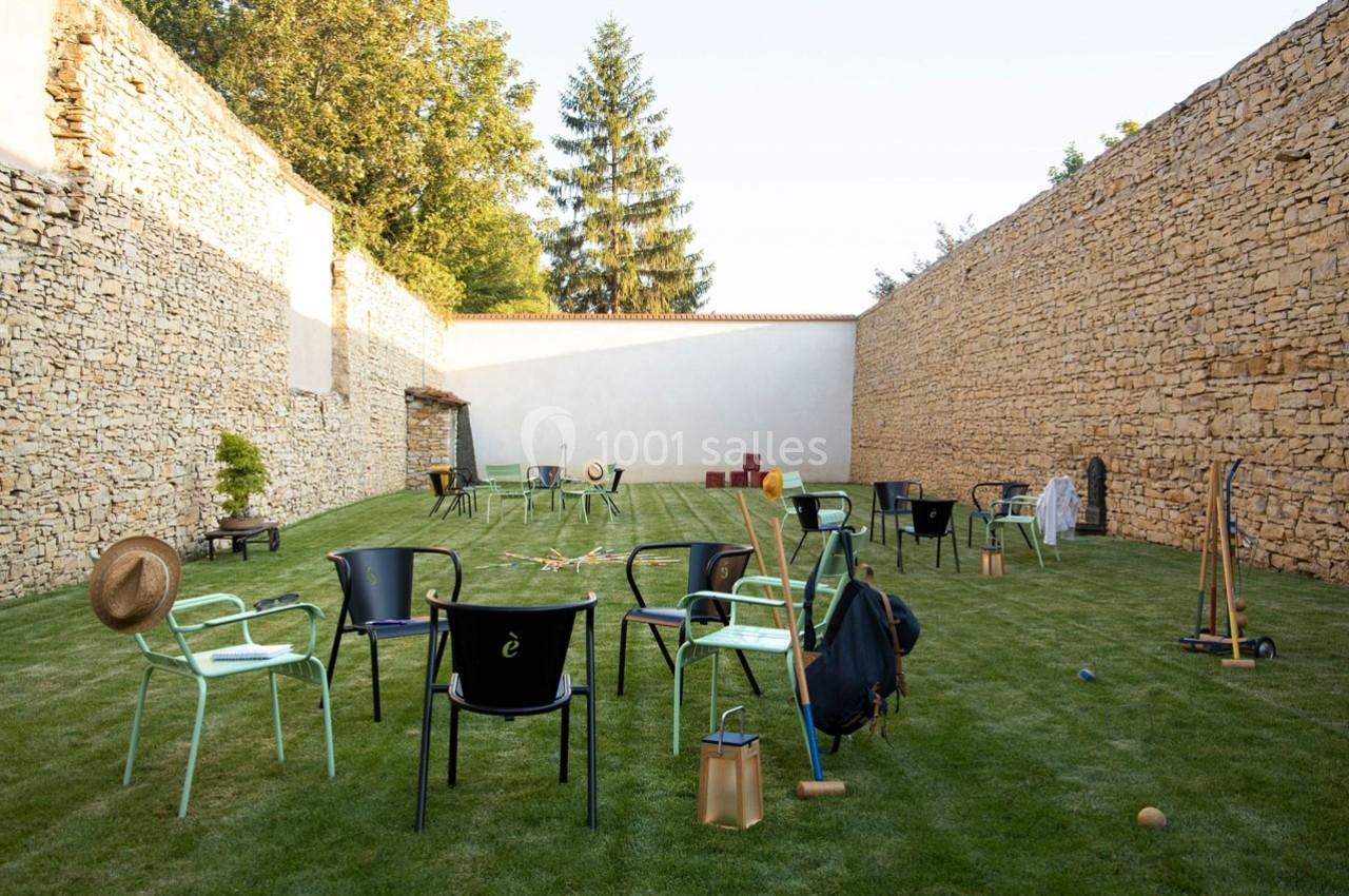 Chaises éparpillées sur une pelouse entourée de murs en pierre, avec des accessoires et jeux d'extérieur.