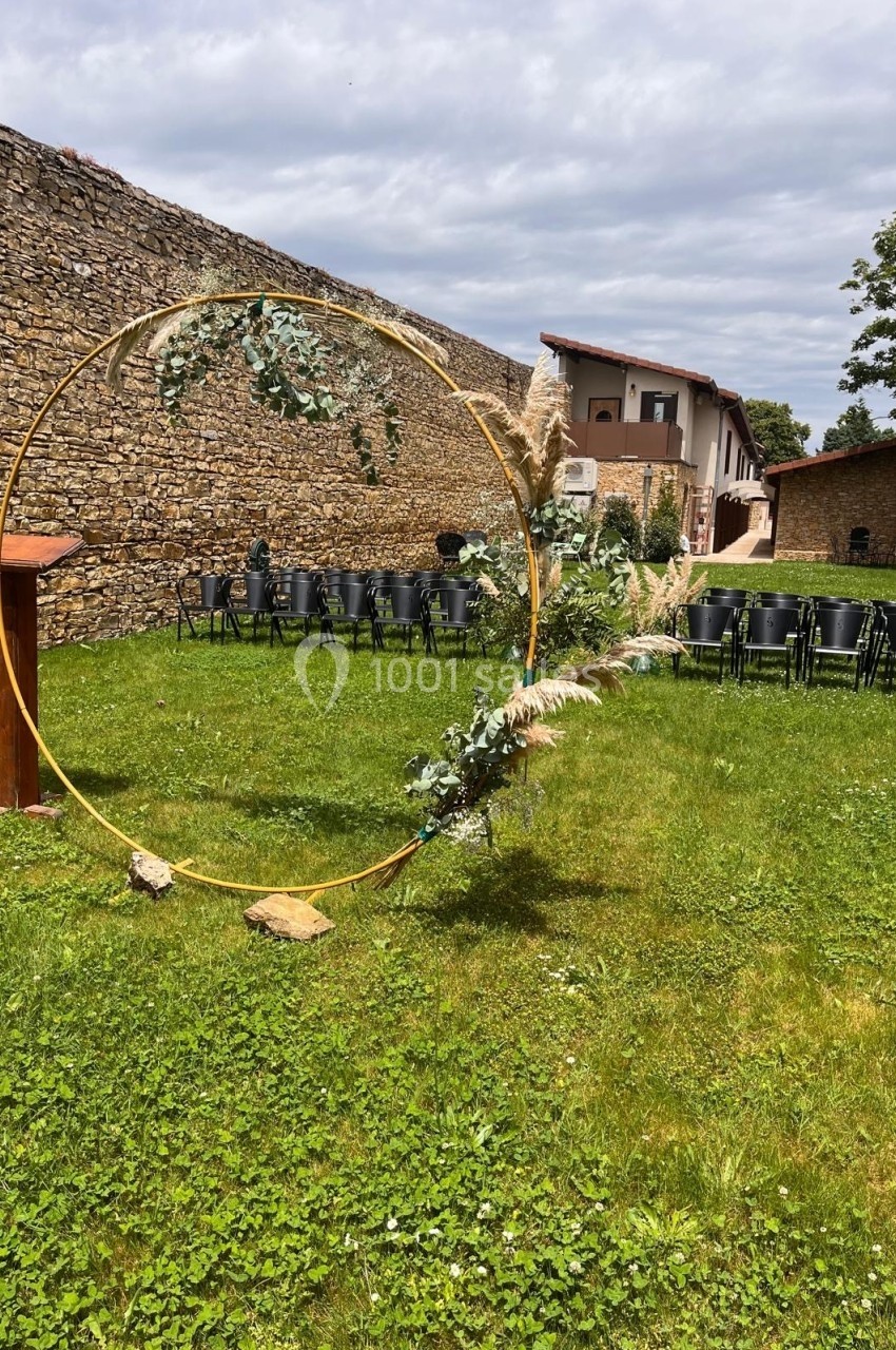 Arche circulaire décorée de feuillages sur une pelouse, avec des chaises noires disposées en arrière-plan.